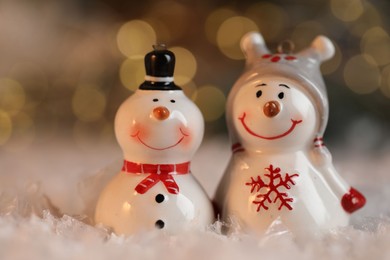 Photo of Funny snowman figures on artificial snow against blurred lights, closeup