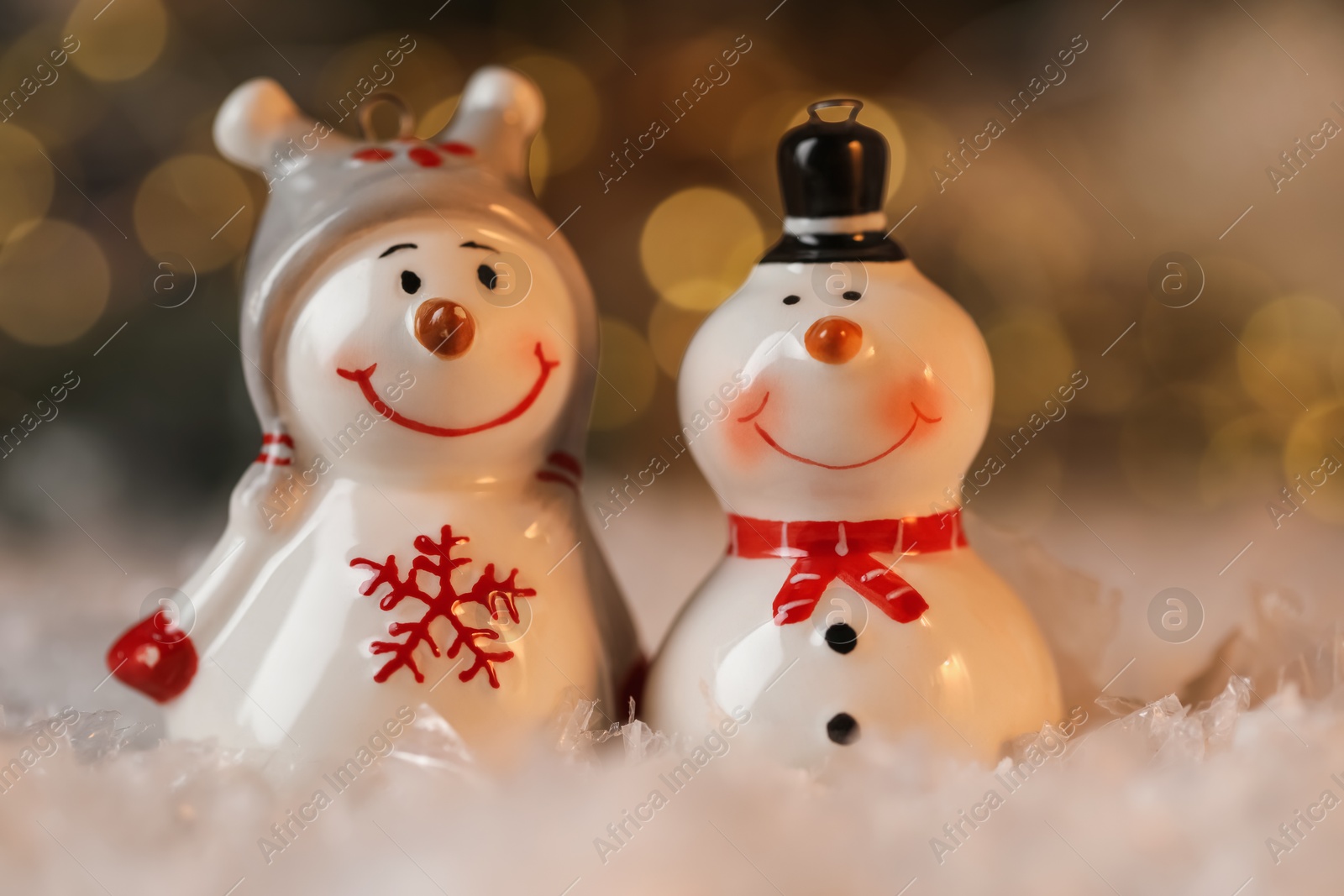 Photo of Funny snowman figures on artificial snow against blurred lights, closeup