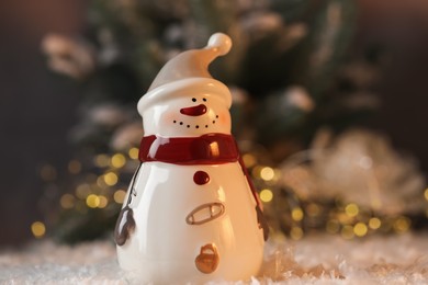 Photo of Funny snowman figure on artificial snow against blurred lights, closeup