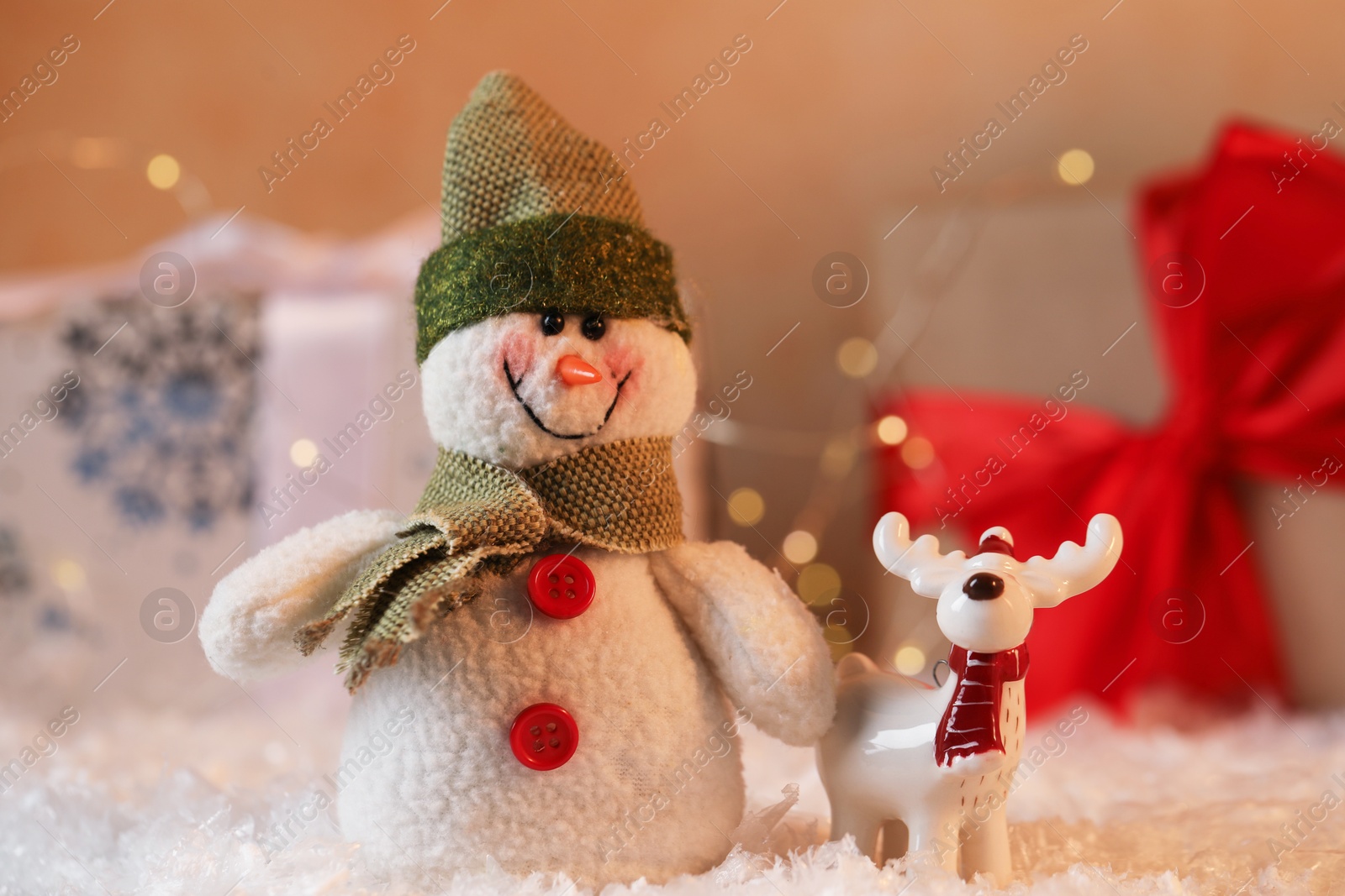 Photo of Funny snowman and deer figures on artificial snow against blurred background