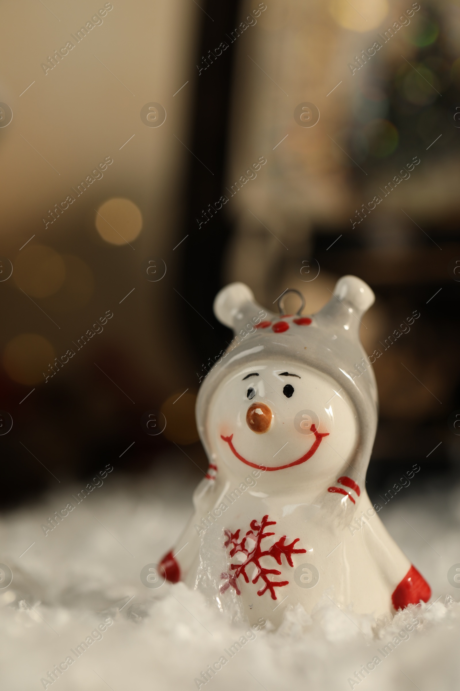 Photo of Funny snowman figure on artificial snow against blurred lights, closeup