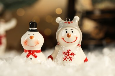 Photo of Funny snowman figures on artificial snow against blurred lights, closeup