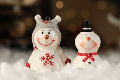 Photo of Funny snowman figures on artificial snow against blurred lights, closeup