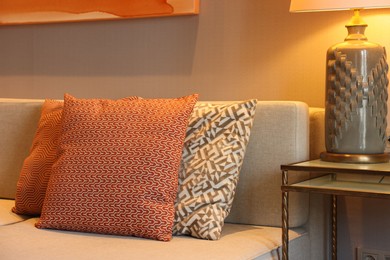 Photo of Comfortable sofa with cushions and lamp on side table in room