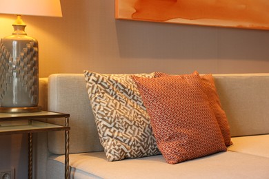 Photo of Comfortable sofa with cushions and lamp on side table in room