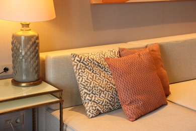 Photo of Comfortable sofa with cushions and lamp on side table in room