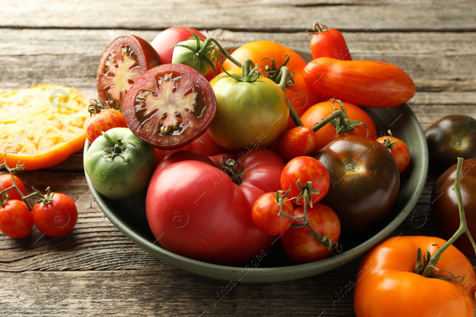 Photo of Different ripe tomatoes in bowl on wooden table, closeup