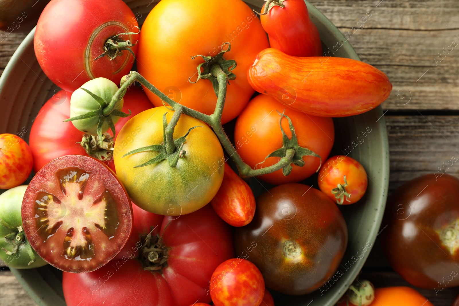 Photo of Different ripe tomatoes in bowl on wooden table, top view