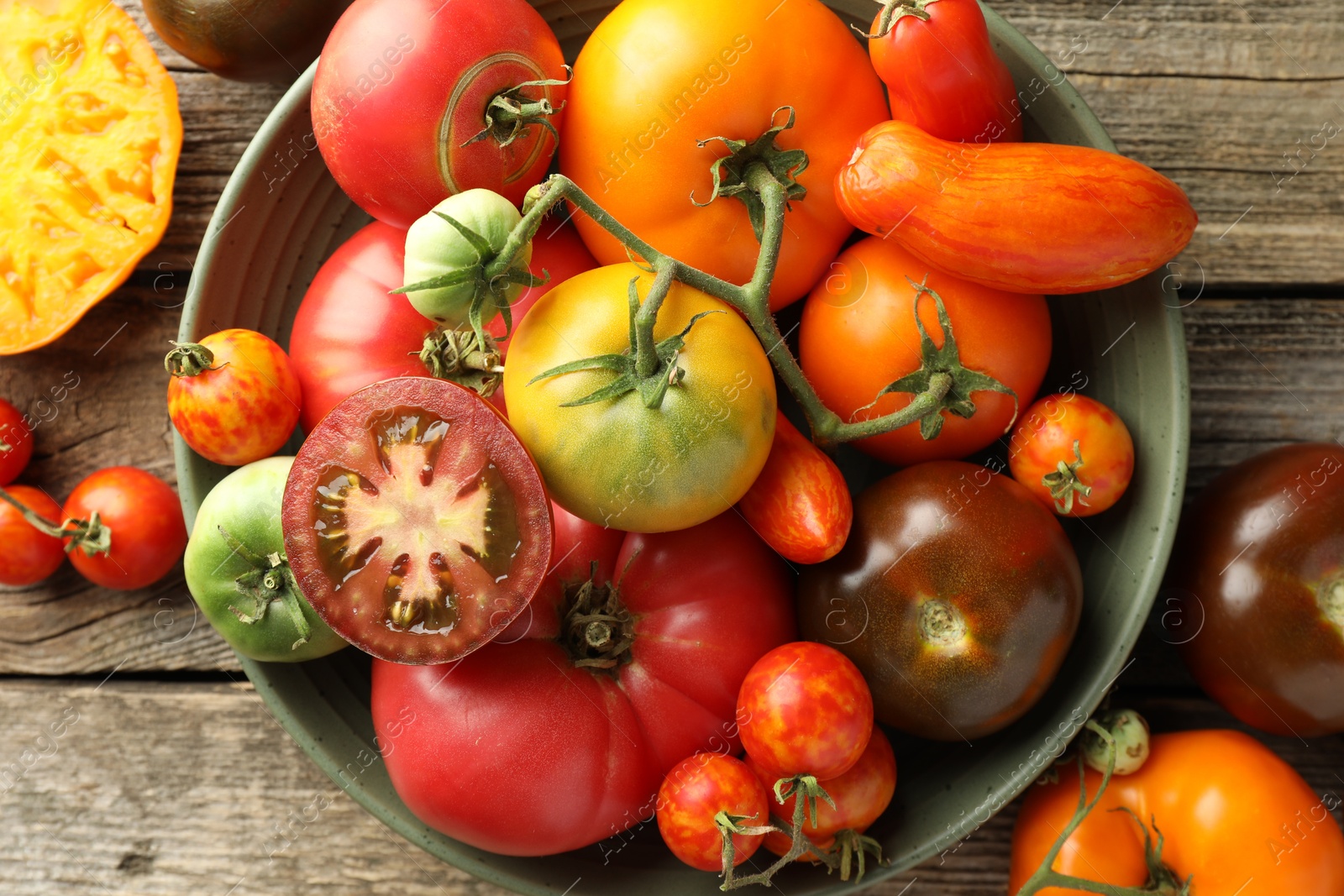 Photo of Different ripe tomatoes in bowl on wooden table, top view