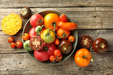 Photo of Different ripe tomatoes in bowl on wooden table, top view