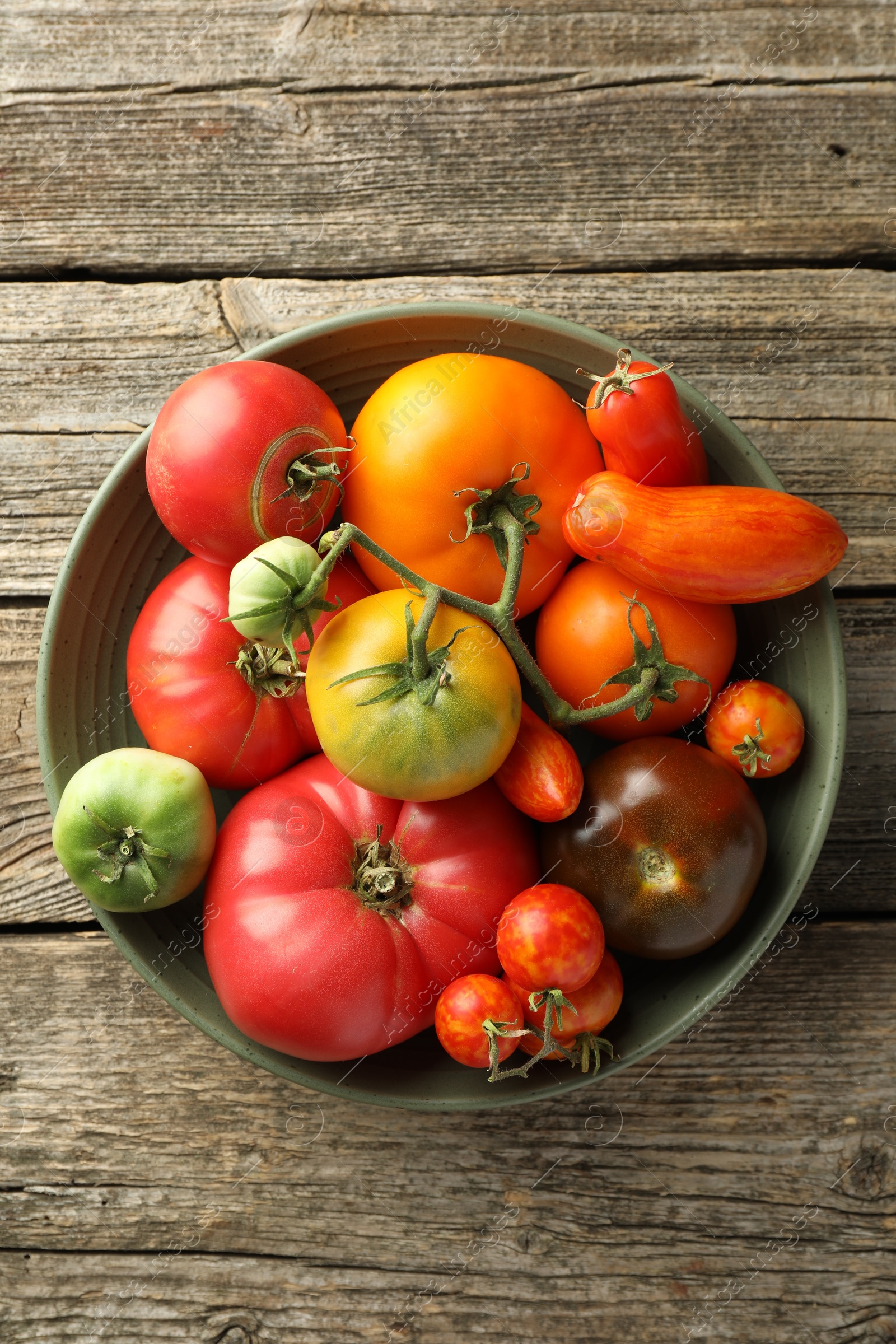 Photo of Different ripe tomatoes in bowl on wooden table, top view