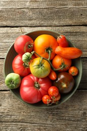 Different ripe tomatoes in bowl on wooden table, top view