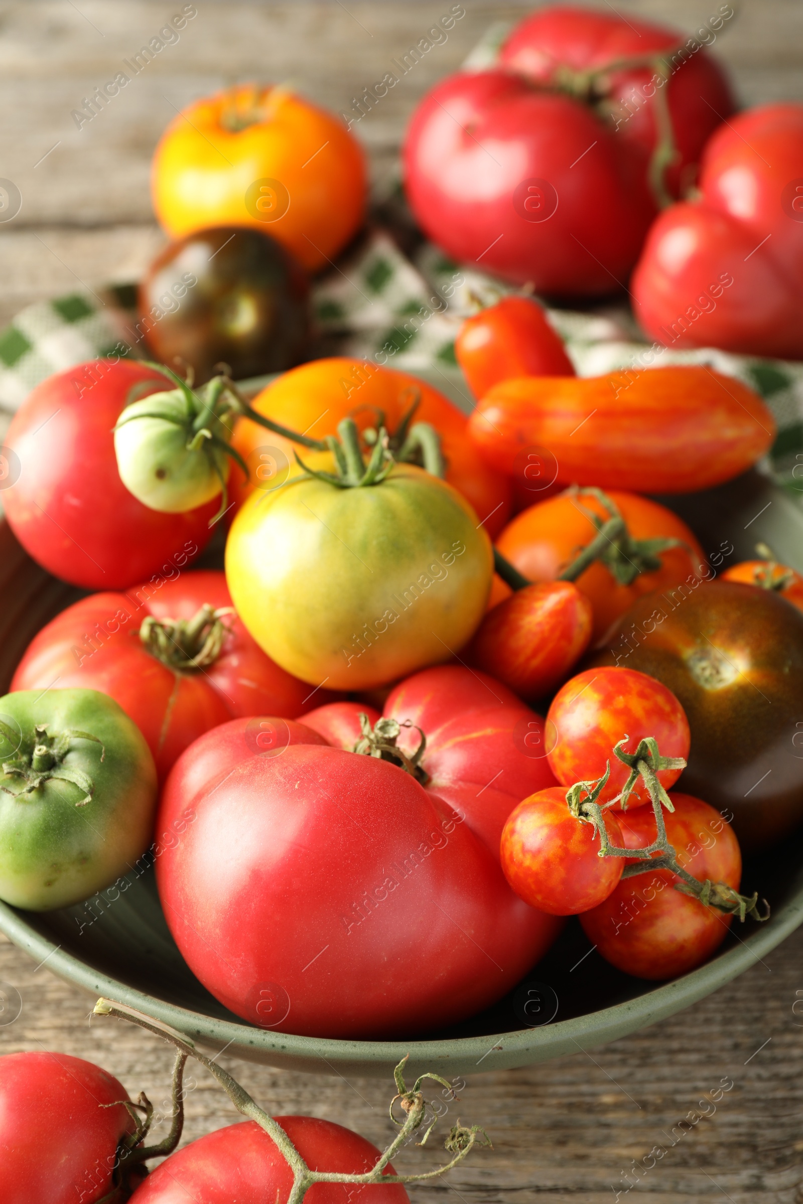 Photo of Different ripe tomatoes in bowl on wooden table, closeup