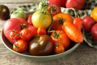 Photo of Different ripe tomatoes in bowl on wooden table, closeup