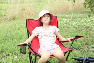 Photo of Cute girl resting in camping chair outdoors