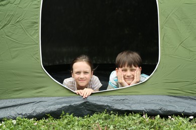 Girl and her brother resting in camping tent on green grass outdoors