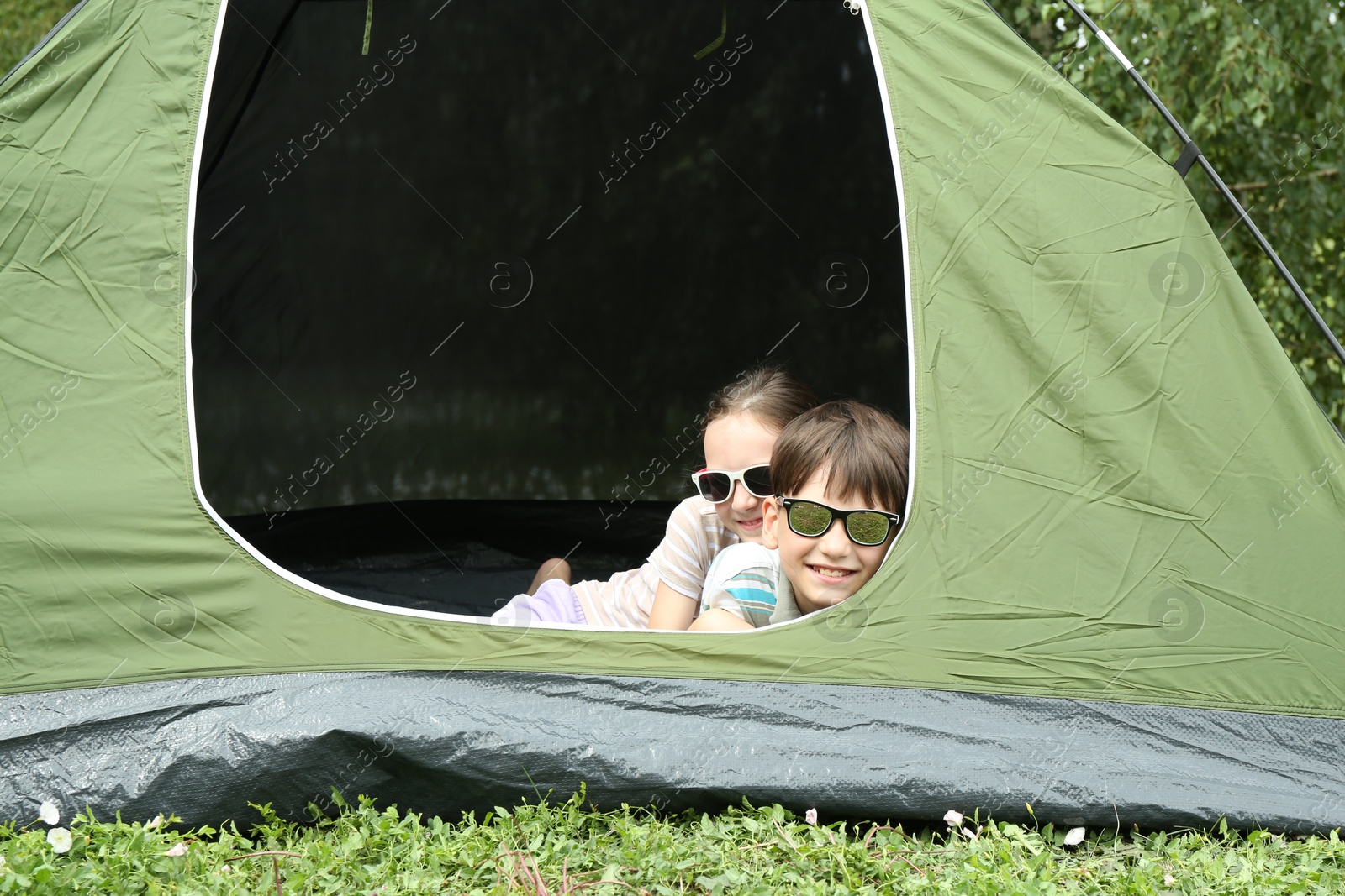 Photo of Girl and her brother resting in camping tent on green grass outdoors