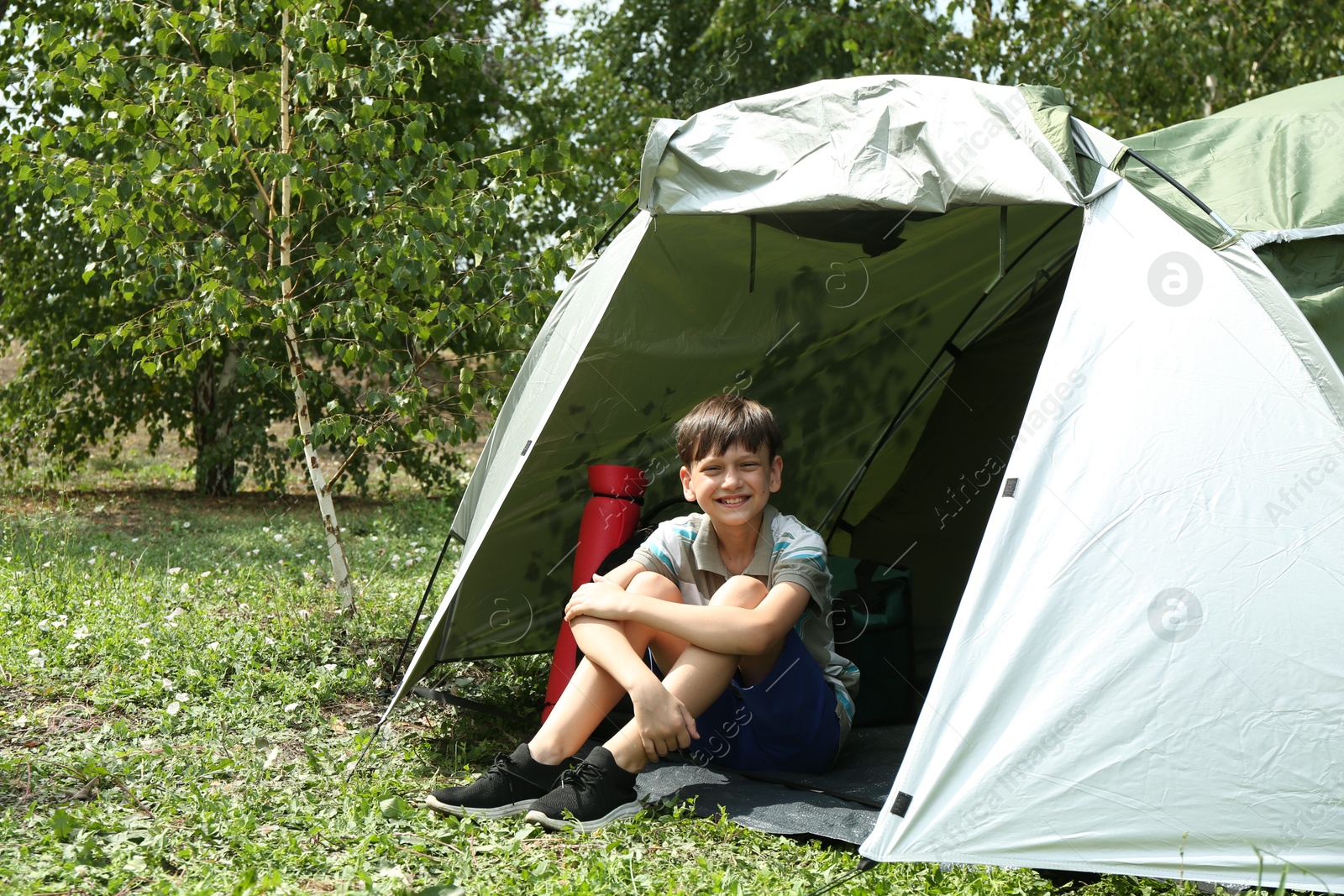 Photo of Cute boy sitting in camping tent outdoors