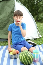 Photo of Boy eating apple near camping tent outdoors