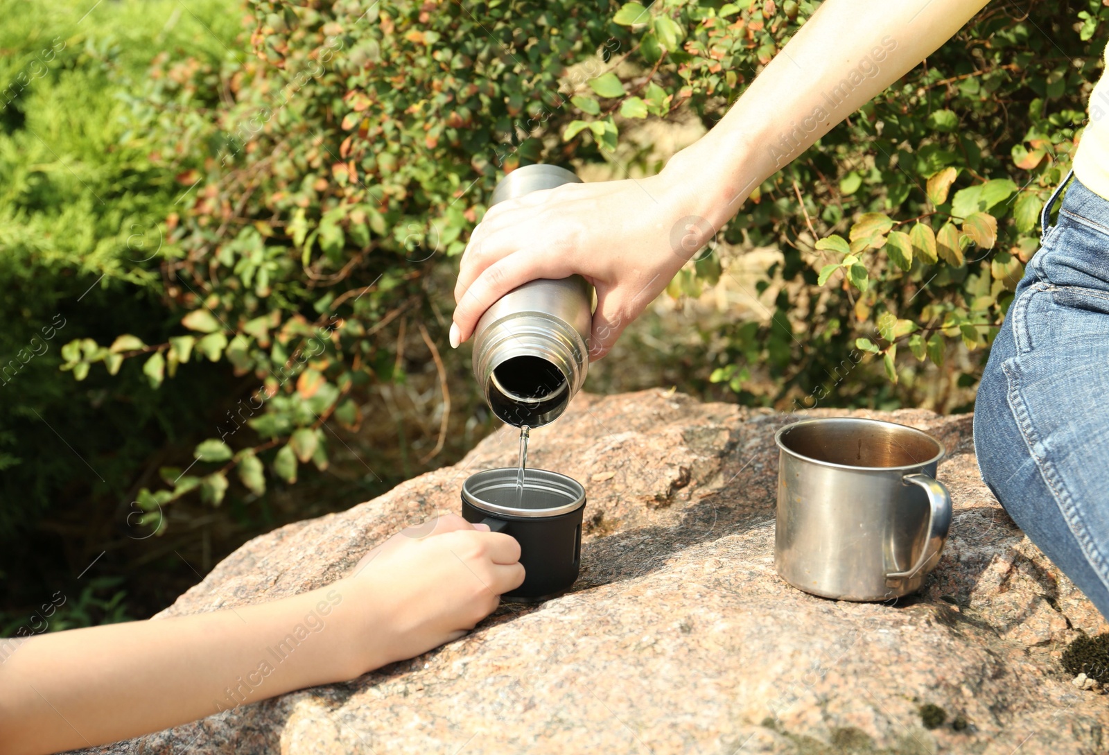 Photo of Mother pouring drink into mug for her daughter outdoors, closeup