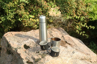 Photo of Thermos and mugs on rock. Camping equipment