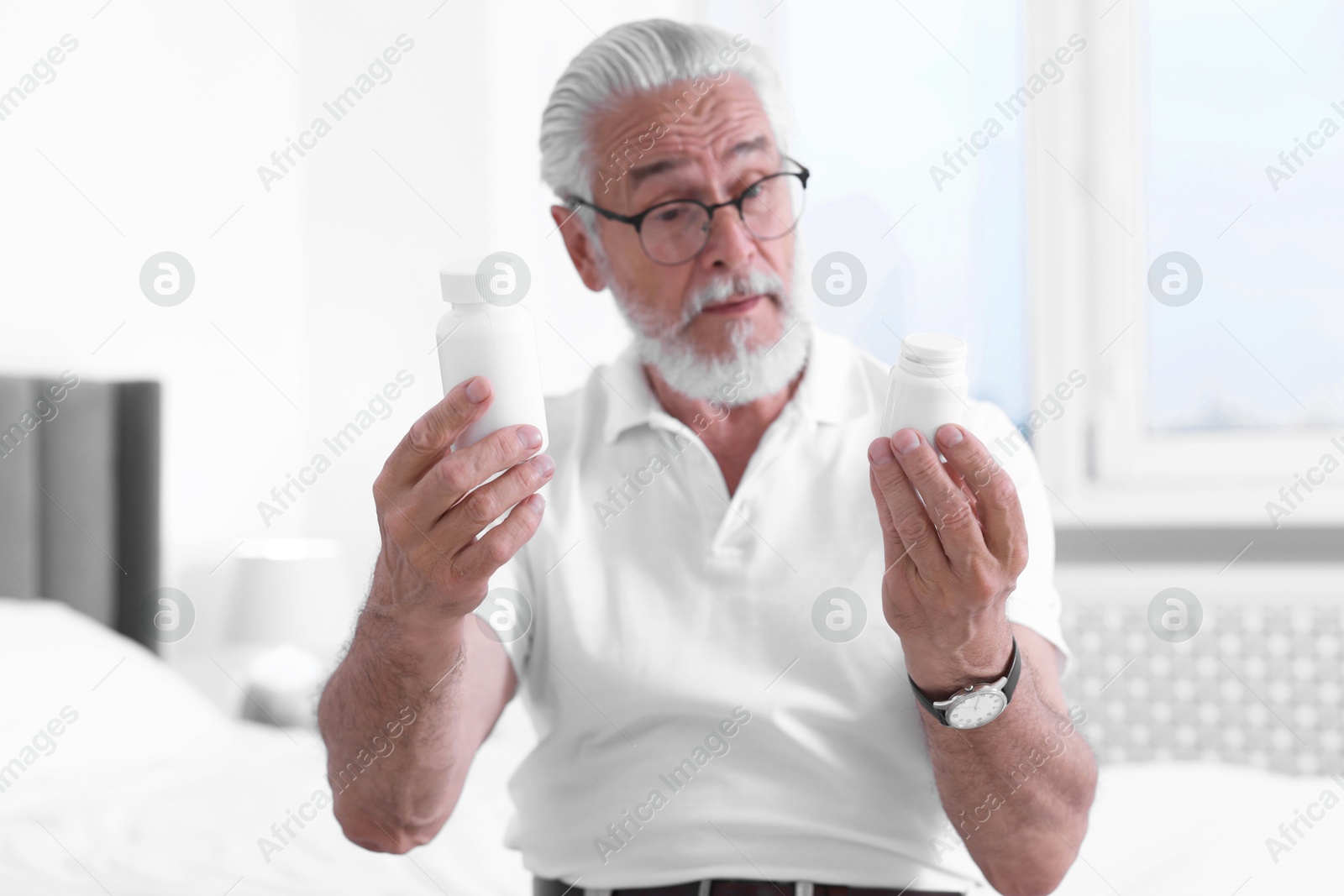 Photo of Senior man with bottles of pills on bed indoors, selective focus