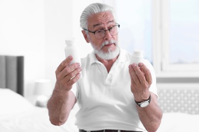 Senior man with bottles of pills on bed indoors, selective focus