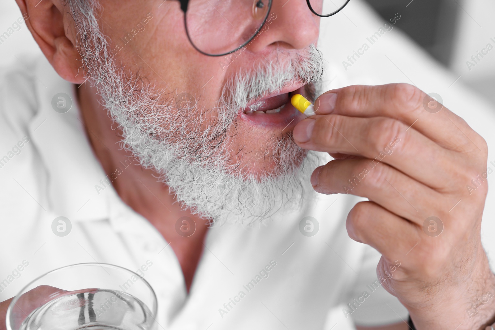 Photo of Senior man with glass of water taking pill at home, closeup