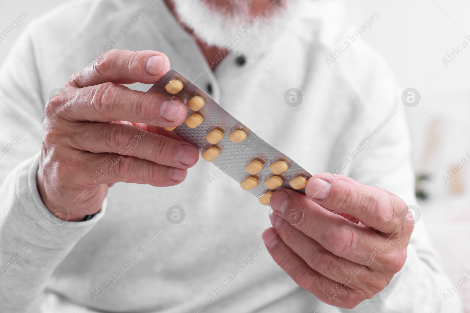 Photo of Senior man holding blister with pills at home, closeup