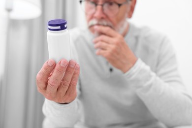 Photo of Senior man with bottle of pills at home, selective focus