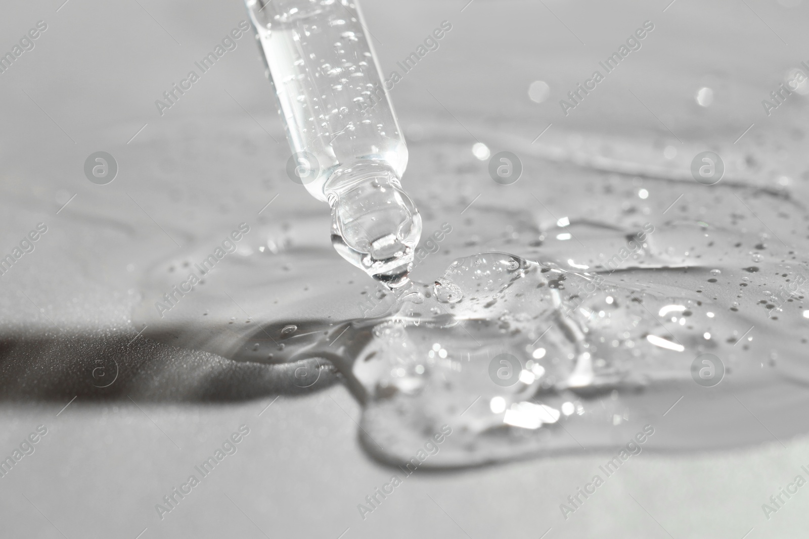 Photo of Dripping cosmetic serum from pipette on grey background, closeup