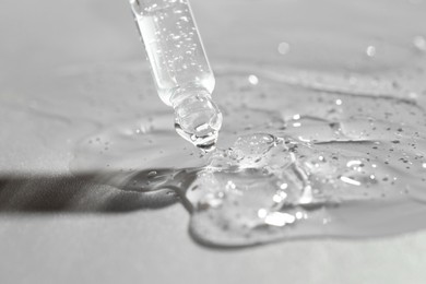 Dripping cosmetic serum from pipette on grey background, closeup