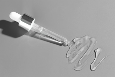 Dripping cosmetic serum from pipette on grey background, top view