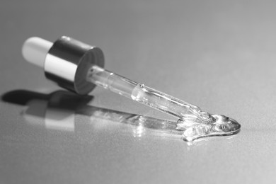 Photo of Dripping cosmetic serum from pipette on grey background, closeup