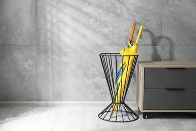 Photo of Holder with bright umbrellas and cabinet indoors. Space for text