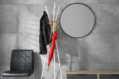 Photo of Red umbrella and jacket on clothing rack at home