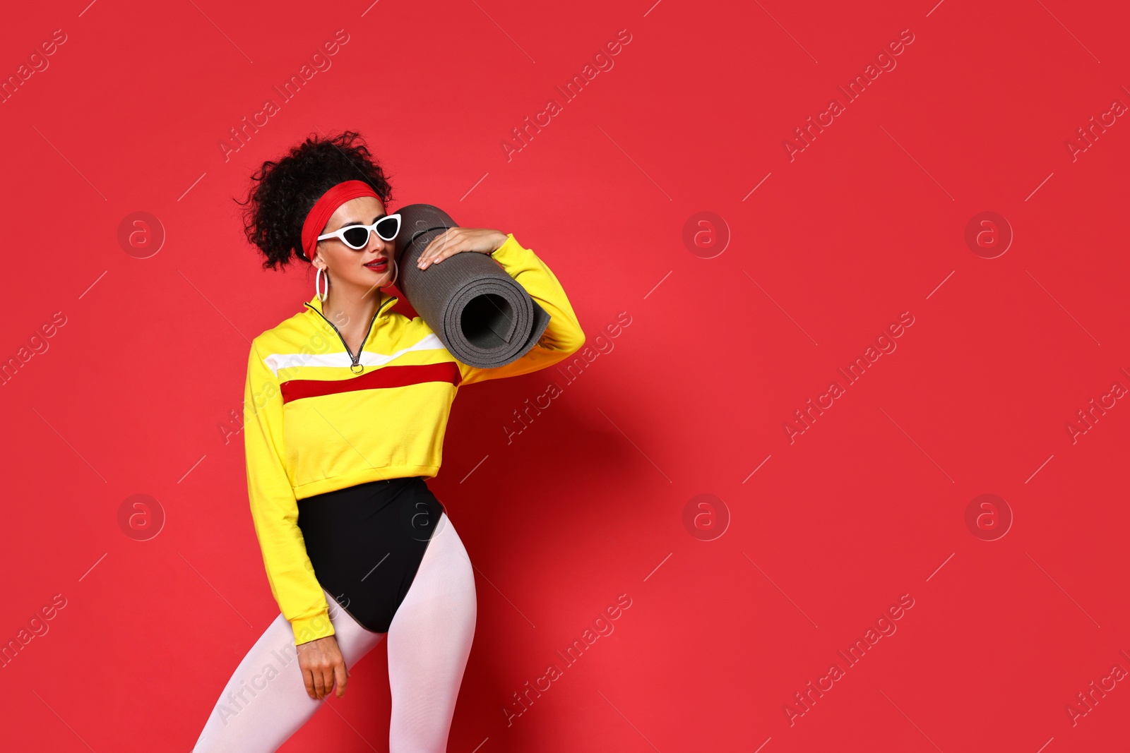 Photo of Aerobics. Woman in sportswear holding fitness mat on red background, space for text