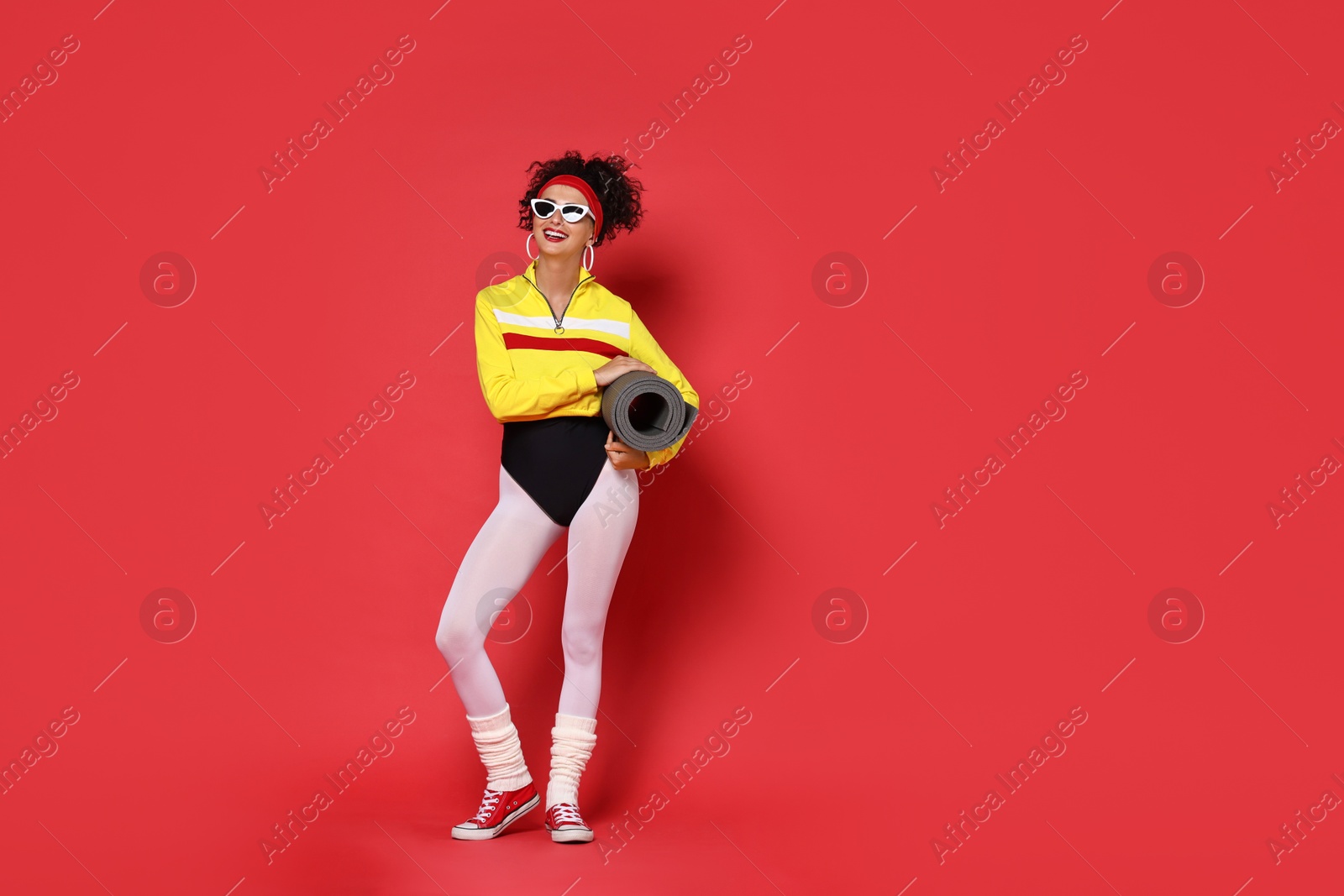 Photo of Aerobics. Woman in sportswear holding fitness mat on red background