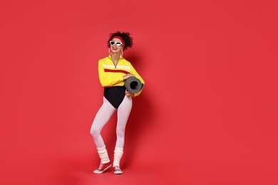 Aerobics. Woman in sportswear holding fitness mat on red background