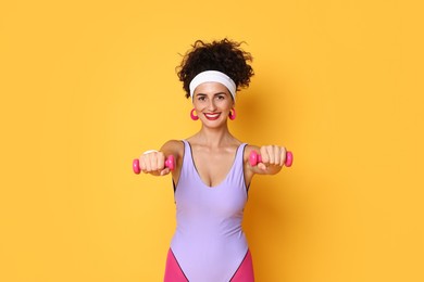 Photo of Woman doing aerobic exercise with dumbbells on orange background