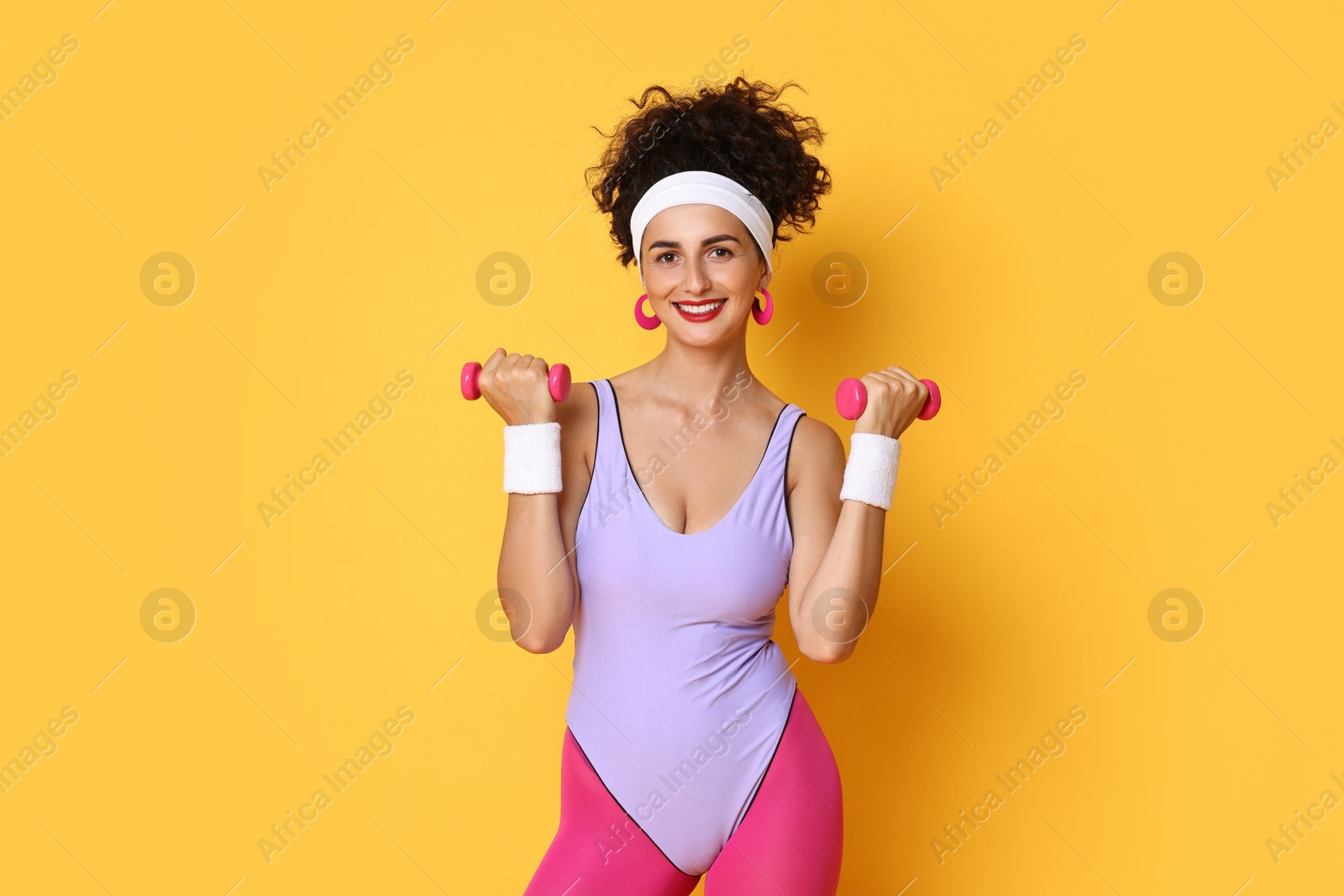 Photo of Woman doing aerobic exercise with dumbbells on orange background