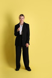 Photo of Beautiful woman in stylish black suit on yellow background