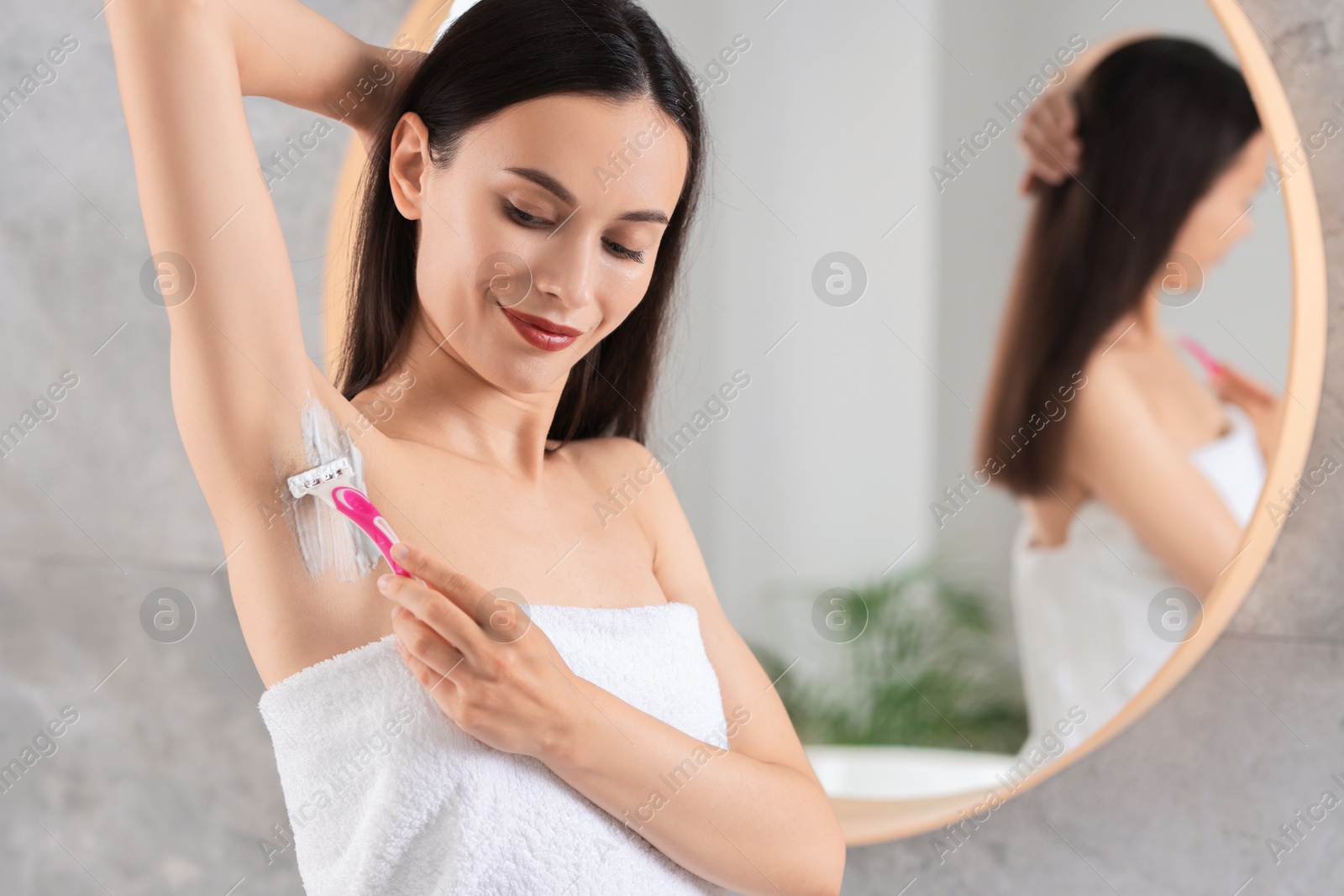 Photo of Beautiful woman shaving armpit near mirror indoors