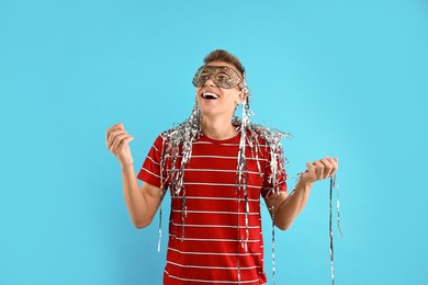 Charming young man wearing carnival mask on light blue background