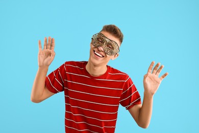 Photo of Charming young man wearing carnival mask on light blue background