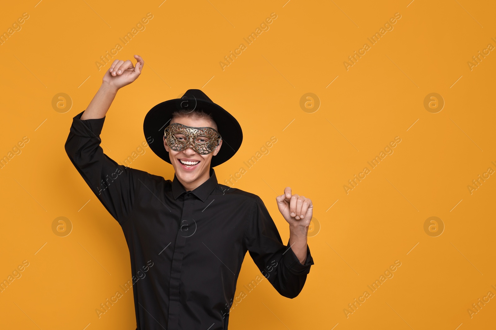 Photo of Charming young man wearing carnival mask on orange background. Space for text