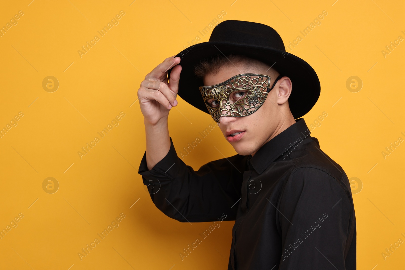 Photo of Charming young man wearing carnival mask on orange background. Space for text