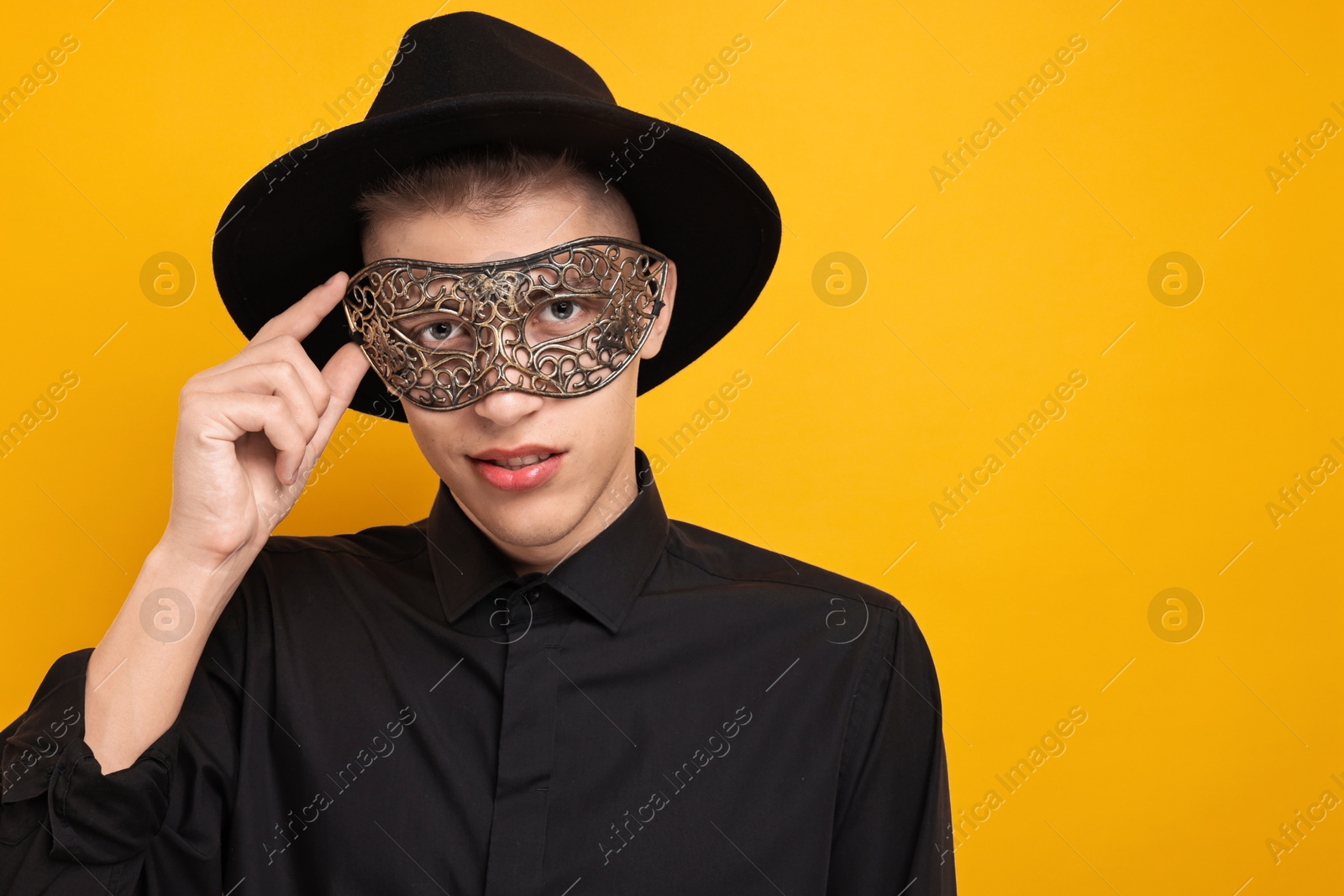 Photo of Charming young man wearing carnival mask on orange background. Space for text