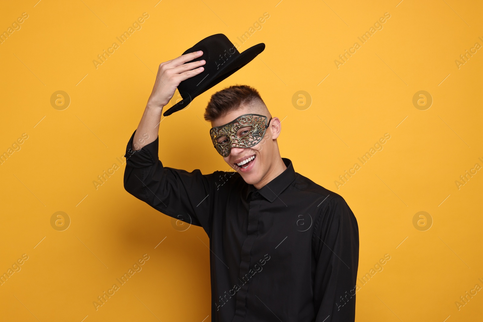 Photo of Charming young man wearing carnival mask on orange background