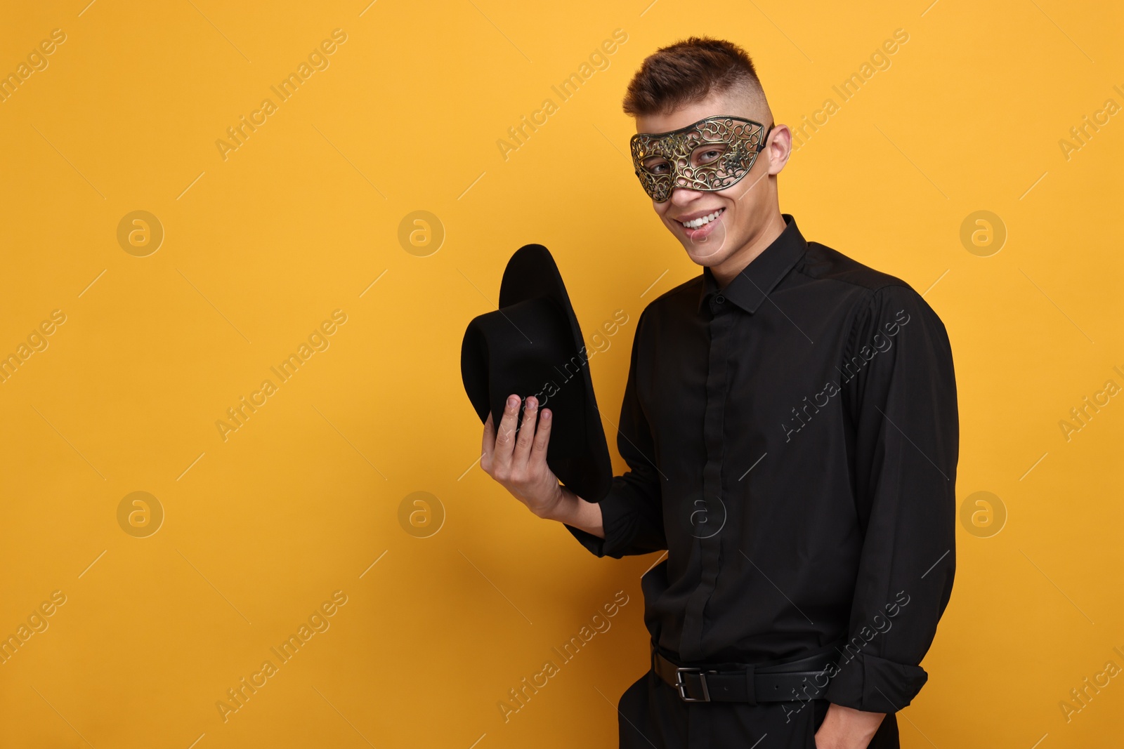 Photo of Charming young man wearing carnival mask on orange background. Space for text